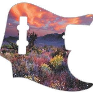 May include: A guitar pickguard with a desert sunset landscape design. The pickguard features a colorful sunset over a desert landscape with mountains and cacti. The pickguard is made of a durable material and is designed to fit most standard guitars.