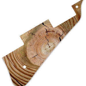 Puede incluir: Una placa de protección de guitarra con un diseño de veta de madera. La placa de protección tiene forma de púa de guitarra y tiene un borde blanco. La veta de madera es de color marrón claro con un centro marrón oscuro.