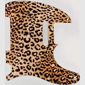 May include: A guitar pickguard with a leopard print pattern. The pickguard is designed to fit a particular guitar model, displaying a mix of tan and brown spots on a light tan base. It has several screw holes for mounting.