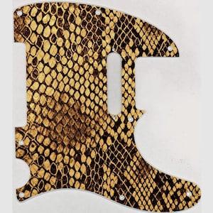 May include: A gold and brown guitar pickguard with a snake skin pattern.