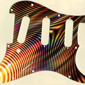 May include: A colorful guitar pickguard with a vibrant, swirling pattern of orange, yellow, red, and purple. The pickguard has three pickup cutouts and several screw holes. The design resembles a psychedelic, abstract artwork.