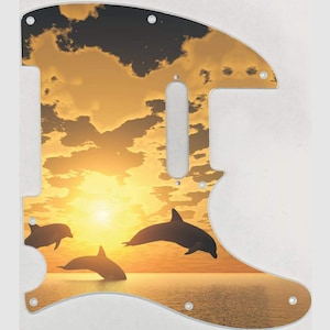 May include: A guitar pickguard with a sunset and dolphin silhouette design. The pickguard is a light brown color with a yellow sunset and three dolphins jumping out of the water. The dolphins are black silhouettes against the sunset.