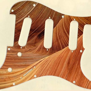 Peut inclure: Un pickguard de guitare avec un motif en bois. Le pickguard est blanc avec un motif en bois brun et orange. Le pickguard a trois trous de micros et un trou de bouton de commande.