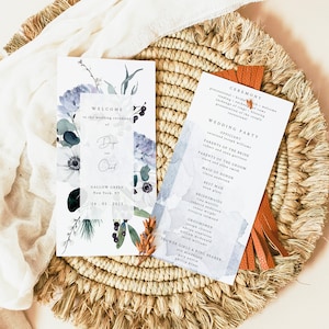 Puede incluir: Un programa de ceremonia de boda con un diseño de acuarela con flores azules y blancas. El programa incluye los nombres de la fiesta de bodas y el orden de los eventos. El texto "Bienvenido a la ceremonia de boda de Dy y Chad" está impreso en la parte delantera del programa.