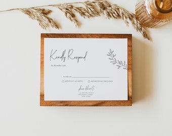 Pode incluir: Um cartão RSVP branco com uma moldura de madeira. O cartão tem um título escrito à mão "Kindly Respond" com uma linha de texto que diz "by December 13th". O convidado tem duas opções para escolher: "Joyfully Accepts" ou "Regretfully Declines". O cartão também inclui o endereço "15 Irving Place, Gramercy Park, New York".