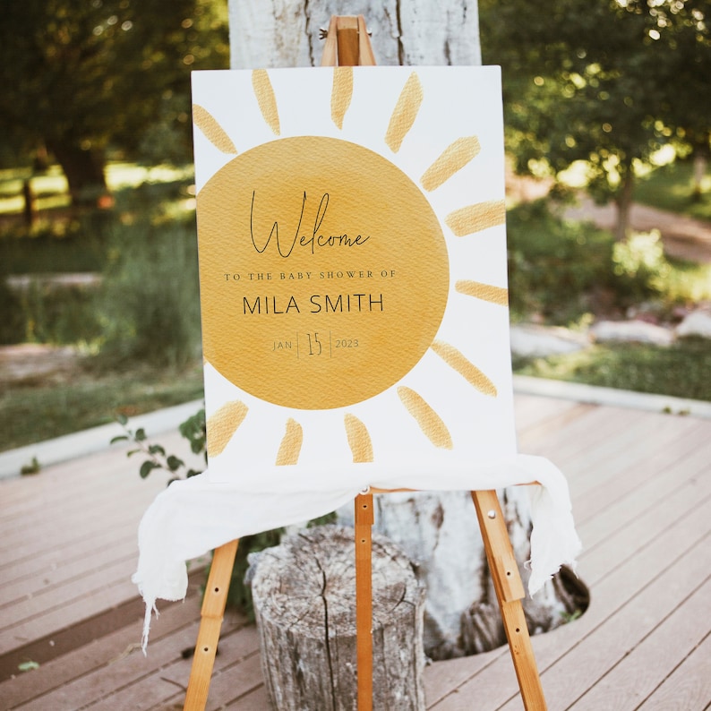 K&ouml;nnte beinhalten: Willkommen zur Babyparty von Mila Smith, ein wei&szlig;es Schild mit einer gelben Sonnengrafik und dem Text "Welcome to the baby shower of Mila Smith Jan 15 2023".