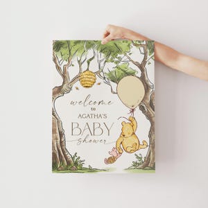 May include: A Winnie the Pooh themed baby shower invitation with a watercolor illustration of Winnie the Pooh holding a balloon and Piglet. The text reads "Welcome to Agatha's Baby Shower".