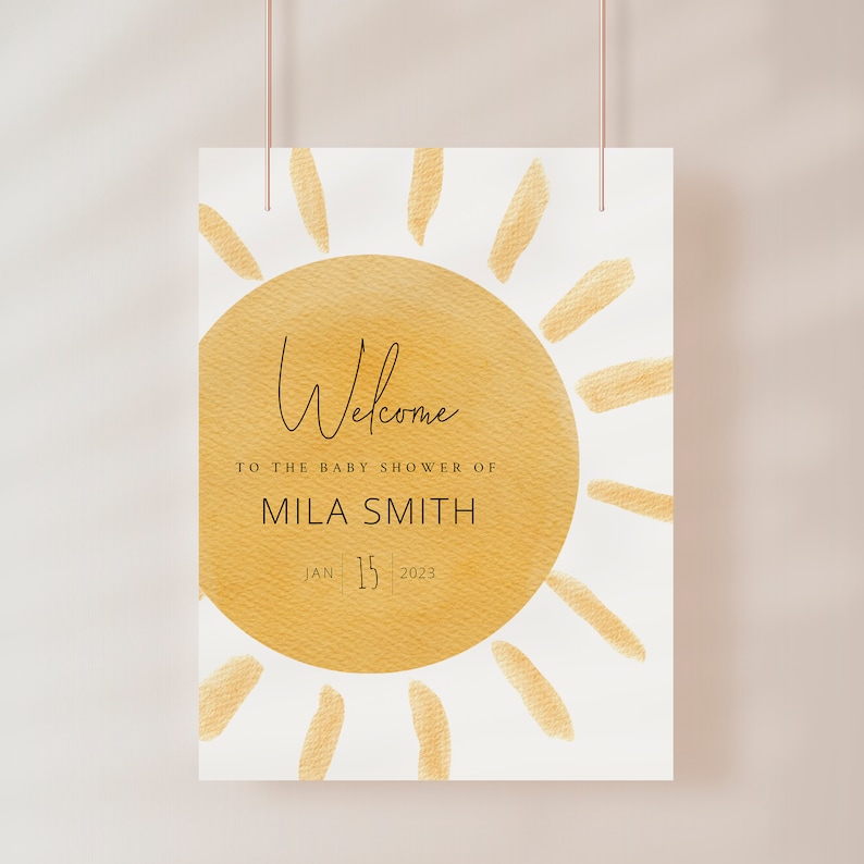 K&ouml;nnte beinhalten: Eine wei&szlig;e Karte mit einem goldenen Sonnenmotiv und dem Text "Willkommen zur Babyparty von Mila Smith Jan 15 2023".
