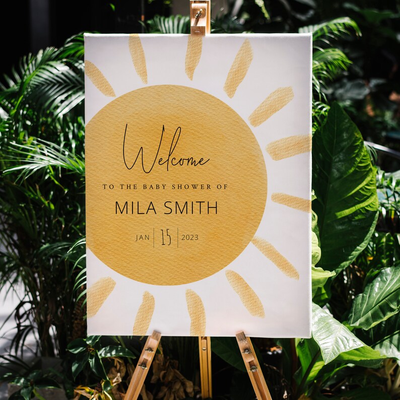 K&ouml;nnte beinhalten: Willkommen zur Babyparty von Mila Smith, ein wei&szlig;es Schild mit einer gelben Sonnengrafik und dem Datum 15. Januar 2023.