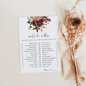 May include: A white card with the text "Would She Rather" and a floral design in burgundy, brown, and green. The card lists various choices for a bridal game, with heart-shaped check boxes.