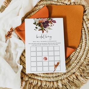 May include: A printable bridal shower bingo card with a floral design in shades of pink, purple, and orange. The card has the text "bridal binge" and "WHAT WILL THE BRIDE-TO-BE RECEIVE?" Fill in the squares with your best guesses. Mark the squares that match as she opens her gifts. First person to get 5 in a row wins!"