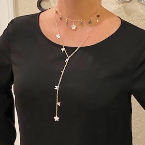 May include: Two gold necklaces with star and letter charms. The longer necklace has a star charm at the bottom and letter charms along the chain. The shorter necklace is a choker with star charms.