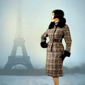 May include: A woman in a tweed suit with a black fur collar and gloves stands in front of the Eiffel Tower. The suit is brown and tan with a matching skirt and jacket, cinched at the waist with a black belt. Black heels complete the look.