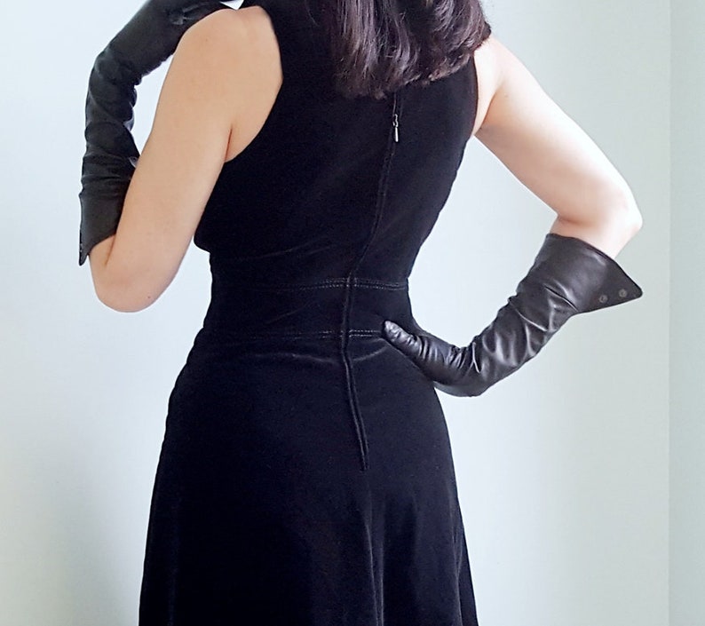 May include: A black velvet dress with a fitted bodice and a flowing skirt. The dress has a zipper in the back and is worn with long black leather gloves.
