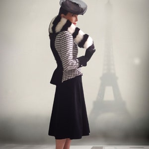 May include: A woman wearing a black and white houndstooth jacket with a black and white fur collar and a black hat. She is standing in front of a blurry image of the Eiffel Tower.