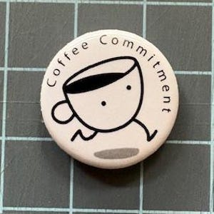 May include: White button with a black outline of a coffee cup with legs and the text "Coffee Commitment" around the cup.