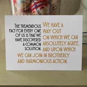May include: A white card with gold text that reads "The tremendous fact for every one of us is that we have discovered a common solution. We have a way out on which we can absolutely agree, and upon which we can join in brotherly and harmonious action."