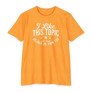 May include: Orange short-sleeved t-shirt with a white graphic that says "I Like This Topic Deliver Us From Ego Est. 2020".