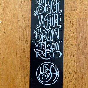 May include: Black sticker with white lettering that reads "Black, White, Brown, Yellow, Red" and a white circle with the letters "USA" inside.