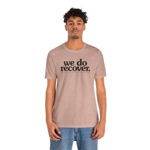 May include: A heathered light brown short-sleeve t-shirt featuring the black text "we do RECOVER." printed on the chest, with smaller text underneath that reads "from a seemingly hopeless state of mind and body."