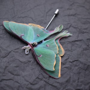 May include: A green and yellow moth pin with a beaded body. The moth is a realistic representation of a Luna moth.