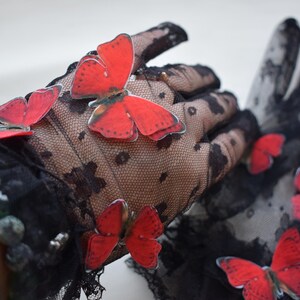 May include: Black lace gloves adorned with vibrant red butterfly appliqu&eacute;s. The gloves feature a delicate floral pattern and are embellished with small, decorative beads. A stylish accessory for special occasions.