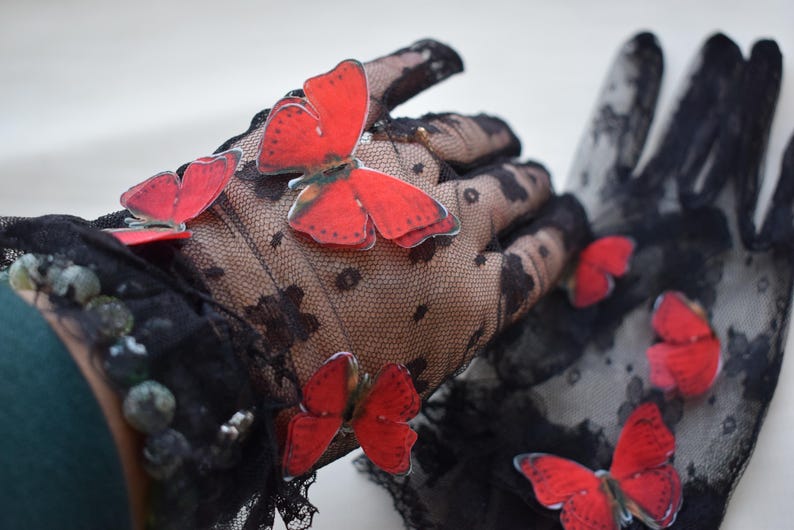 May include: Black lace gloves adorned with vibrant red butterfly appliqu&eacute;s. The gloves feature a delicate floral pattern and are embellished with small, decorative beads. A stylish accessory for special occasions.