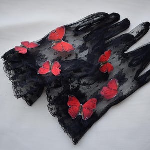 May include: A pair of black lace gloves adorned with vibrant red butterfly appliqu&eacute;s. The gloves have a delicate, floral lace pattern and scalloped edges. The butterflies are evenly spaced across the gloves.
