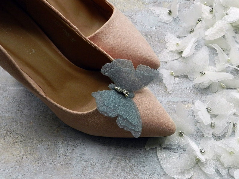 May include: A pair of light pink suede high heels with a delicate blue butterfly embellishment on each shoe. The butterflies have a rhinestone accent.