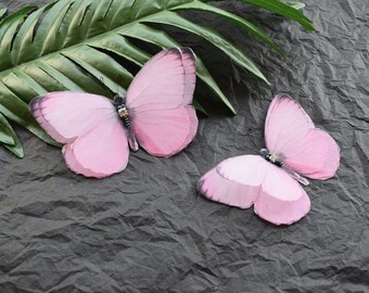 May include: Two pink butterfly decorations with beaded accents on a gray textured background.