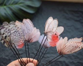 May include: Set of six butterfly hair clips with black metal pins. The butterflies are made of translucent fabric with delicate wing patterns and some have red accents.