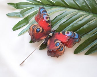 May include: A red, black, and blue butterfly brooch with a silver pin. The butterfly is made of layered fabric and has a beaded accent.