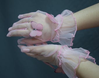 May include: Sheer pink gloves with delicate butterfly accents. The gloves feature a ruffled trim in a matching pink hue. The butterflies are also pink and add a whimsical touch to the design. A feminine accessory.