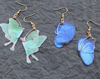 Puede incluir: Un par de pendientes de mariposa dorados con alas verdes y azules. Los pendientes están hechos de resina y tienen un aspecto delicado y femenino.