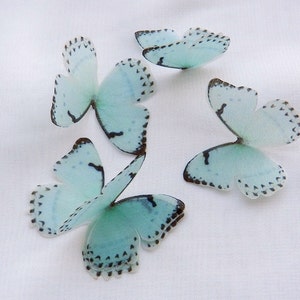 May include: Five light blue butterflies with black markings on a white background. The butterflies are made of a delicate material and have a translucent appearance.