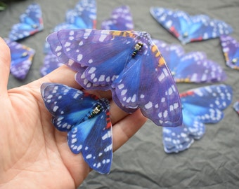 May include: A set of blue and purple butterfly appliques with white spots and iridescent accents. The appliques are made of sheer fabric and have a delicate, whimsical look.