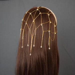 Op de afbeelding: Gouden ketting hoofdband met kristallen kralen. De ketting is ontworpen in een web-achtig patroon met hangende kettingstrengen en kralen.