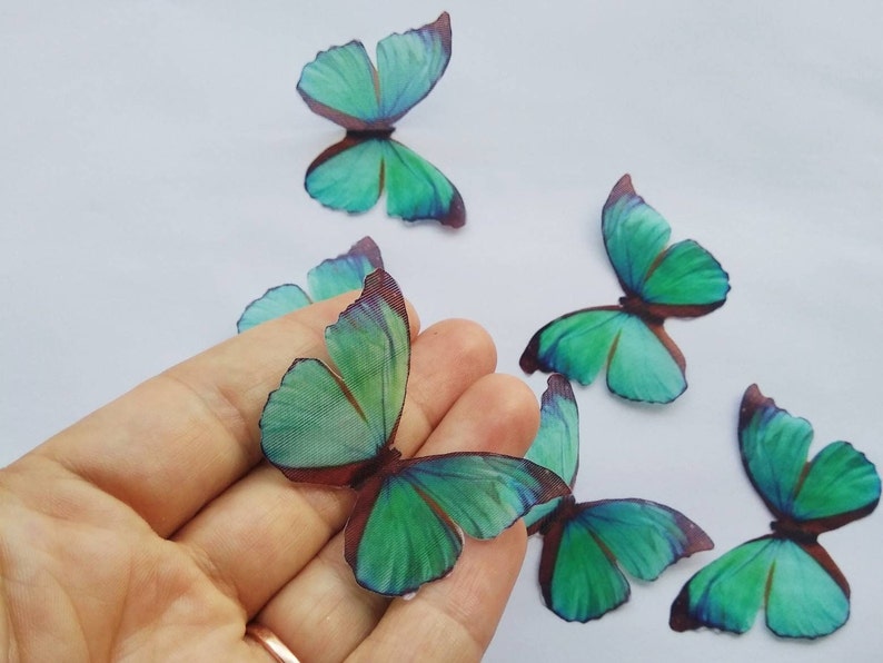 May include: Six teal blue butterfly embellishments with brown veins. The butterflies are made of a translucent material and have a delicate, ethereal appearance.