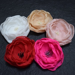 May include: Five fabric flower hair clips in different colors, including white, pink, red, and fuchsia. Each flower has a pearl or rhinestone embellishment in the center.
