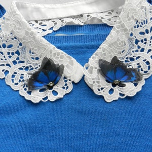 K&ouml;nnte beinhalten: Ein blauer Pullover mit einem wei&szlig;en Spitzenkragen und zwei blauen Schmetterlingsbroschen.