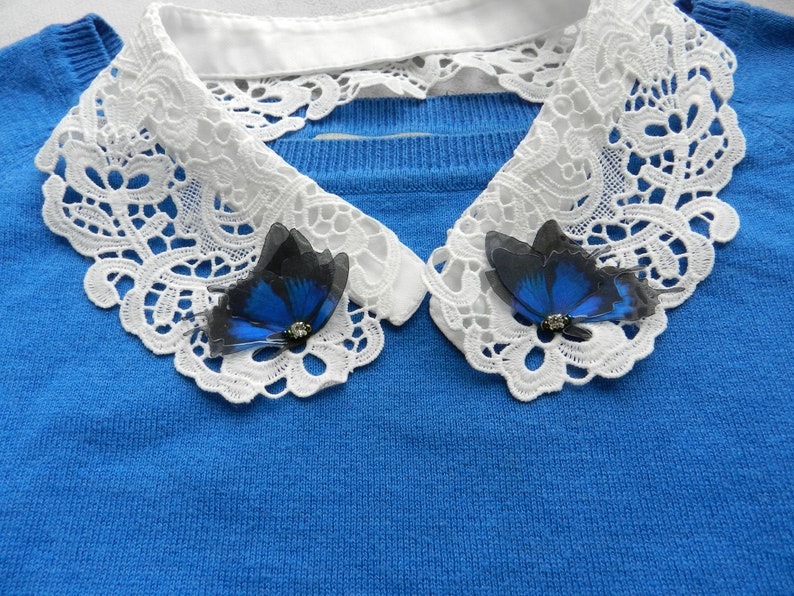 K&ouml;nnte beinhalten: Ein blauer Pullover mit einem wei&szlig;en Spitzenkragen und zwei blauen Schmetterlingsbroschen.