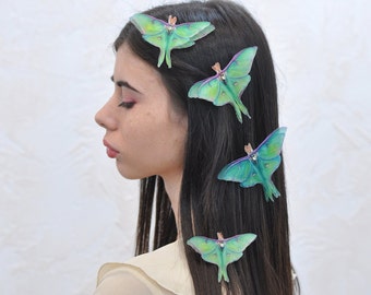 May include: A woman with long dark hair has four green and blue butterfly hair clips in her hair. The butterfly clips are iridescent and have a delicate design.