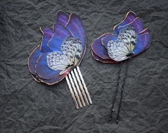 May include: Two butterfly hair clips, one with a comb and the other with two bobby pins. The butterflies are made of layered iridescent blue and purple fabric with white wings and black accents.