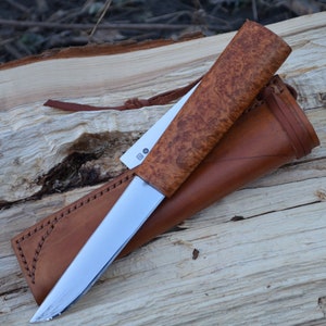 May include: A brown leather sheath with a brown wood handle knife with a silver blade. The knife is on a piece of wood.