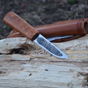 May include: A handmade knife with a wooden handle and a leather sheath. The blade is made of steel and has a hammered finish.