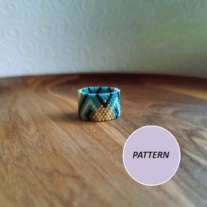 Könnte beinhalten: Ein türkisfarbener, schwarzer, weißer und goldener Perlenring mit geometrischem Muster. Der Ring liegt auf einer Holzoberfläche mit dem Wort "PATTERN" auf einem lila Kreis.