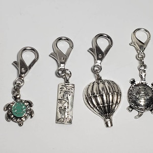 May include: Four silver charm keychains with different designs. The charms include a hot air balloon, a palm tree, and two turtles with turquoise accents.