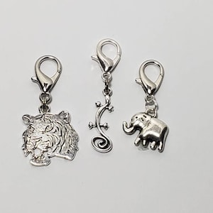 May include: Three silver charm clips with animal designs. The first clip features a tiger head, the second a stylized lizard, and the third an elephant.