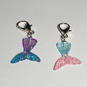 May include: Two iridescent mermaid tail charms with silver lobster clasps. The tails are blue and pink with glitter accents.