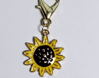 May include: A gold-toned metal charm with a sunflower design. The sunflower has yellow petals and a black center.